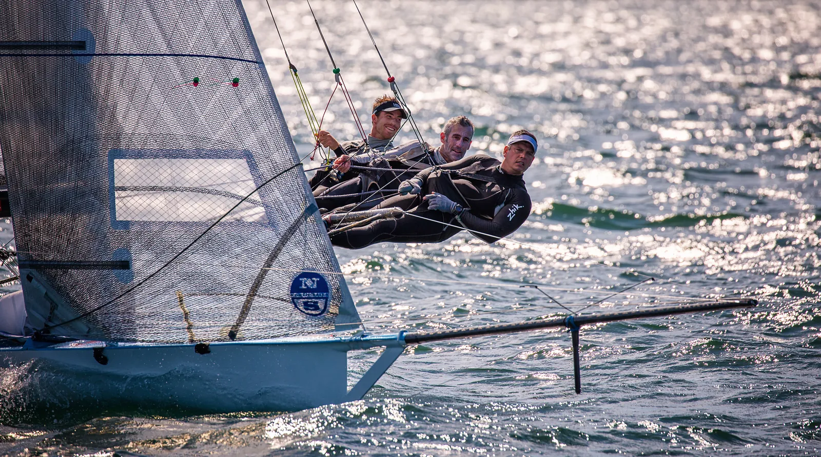 A crew of three hiking out on a racing dinghy